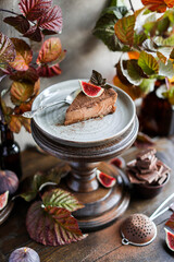 A slice of chocolate cheesecake with fresh figs on a high wooden stand among autumn raspberry leaves. Still life with sweets and natural materials