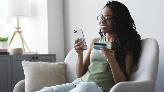 	
Woman holding credit card and using smartphone at home, african american woman shopping online, e-commerce, internet banking, spending money, working from home concept