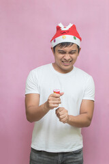 Asian man wearing santa claus hat celebrating christmas with explosive confetti on pink background