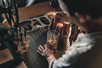 An expert bartender mixing a cocktail in a glass mixer with a long spoon, standing behind the counter of his beautiful cocktail bar in a night club.
