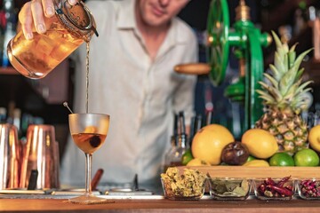 A professional bartender pouring a cocktail in a glass from a shaker and mixer, view of a barman working in a bar.