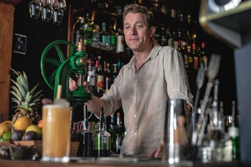A professional bartender working in a fancy cocktail bar serving a colourful tropical drink while standing behind the counter in a night club.