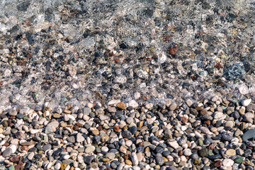 Small color wet pebbles on sea shore. Close-up view from above. Texture, wallpaper, background.