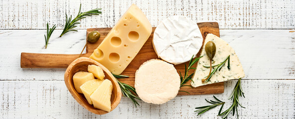 Fototapeta na wymiar Set or assortment cheeses. Suluguni with spice, camembert, blue cheese, parmesan, maasdam, brie cheese with rosemary and pepper. On white wooden old background. Top view. Copy space. Banner.