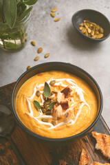 Pumpkin traditional soup with creamy silky texture with sage leaves and red pepper in black plate or bowl. Old grey background. Copy space. Mock up. Top view, flat lay.