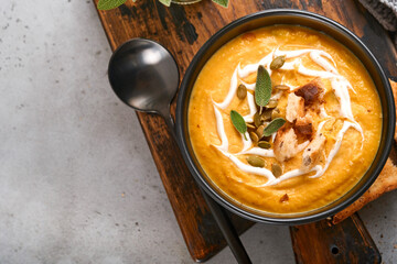 Pumpkin traditional soup with creamy silky texture with sage leaves and red pepper in black plate or bowl. Old grey background. Copy space. Mock up. Top view, flat lay.