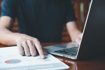 Businessman working on computer laptop and pointing business reports on wood desk at living room concept. Documents summary chart diagram, graph. technology financial analysis, search job