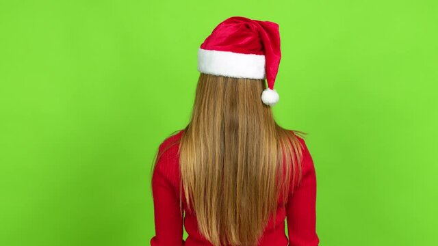 Teenager girl with christmas hat pointing back with the index finger over isolated background