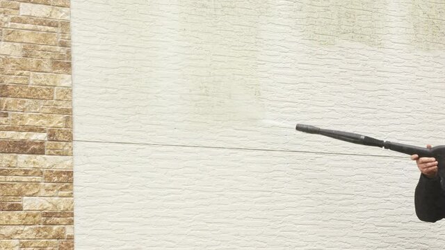 Man cleaning walls with high pressure power washer. Washing cladding walls house.