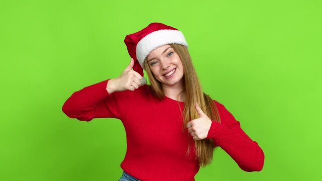 Teenager girl with christmas hat giving thumbs up and smiling because something good has happened over isolated background. Green screen chroma key