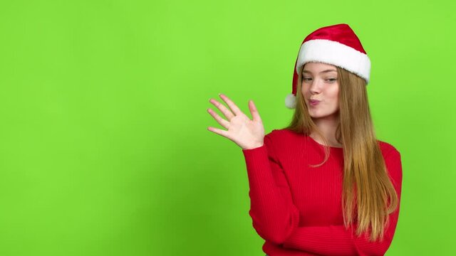 Teenager girl with christmas hat extending hands to the side and inviting to come over isolated background. Green screen chroma key
