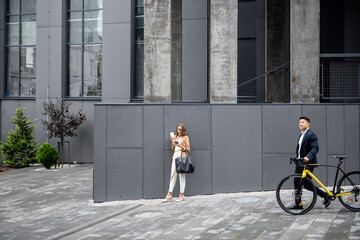 Asian businessman going with bicycle on background of caucasian businesswoman in city. Concept of remote and freelance work. Idea of modern transportation. Young woman with coffee using smartphone
