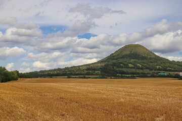 Fototapeta na wymiar A view to the hill Oblik surrounded by fields and blue sky above near Louny, Czech republic