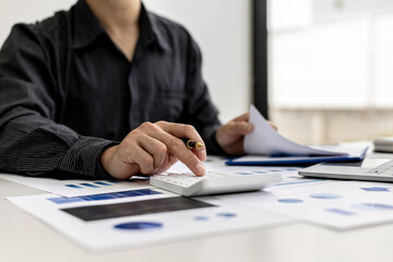Close-up view A businessman using a calculator to calculate numbers on a company's financial...