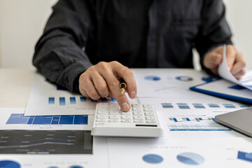 Close-up view A businessman using a calculator to calculate numbers on a company's financial documents, he is analyzing historical financial data to plan how to grow the company. Financial concept.