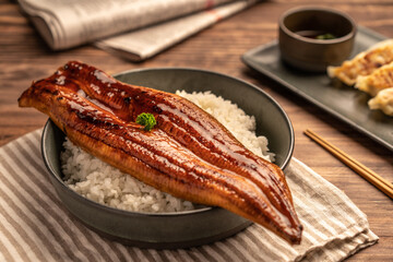๋Close-up Japanese grilled eel served over rice or Unagi don set on plate. Japanese food on restaurant table