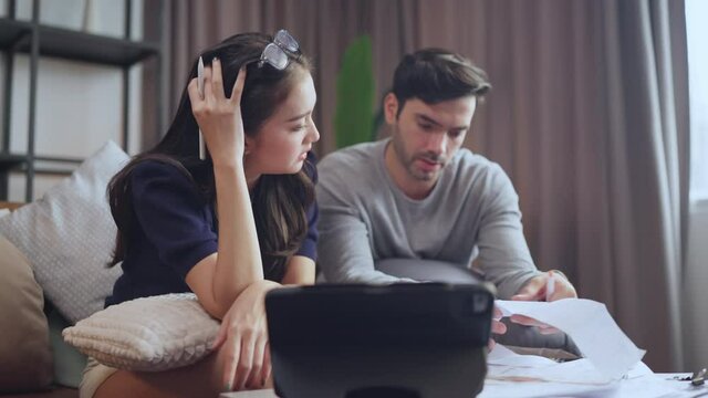 young asian caucasian couple checking bills,discussing planning budget together,serious wife and husband looking attablet screen,online banking services and paper mail bills, checking finances