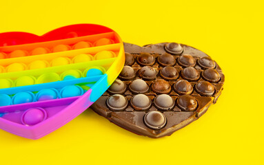 Pop it children's anti-stress toy and a pop it chocolate bar on a bright yellow background. Using pop it as a mold for chocolate. Side view, selective focus