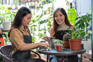 Two Asian friends planting trees, sitting and watering the plants together in the backyard. Hobby idea. 