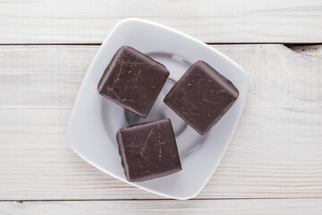 Three sweet chocolates with a saucer on a wooden table, close-up, top view.