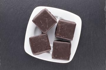 Several sweet chocolates with a white saucer on a slate stone, close-up, top view.