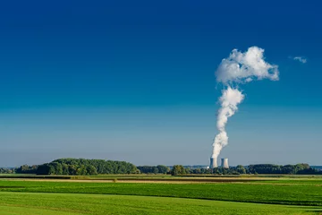 Fotobehang Blick auf Atomkraftwerk, AKW, Gundremmingen, mit blauem Himmel und hoher Rauchsäule eines Kühlturms, Wiesen und Felder im Vordergrund © JM Soedher