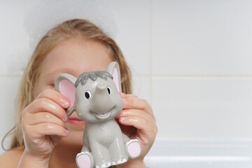 A cute, beautiful, cheerful little girl with long hair is playing in the bathroom with an elephant. Children's emotions in the bathroom. Children's hygiene. Water games. The child washes the toy.