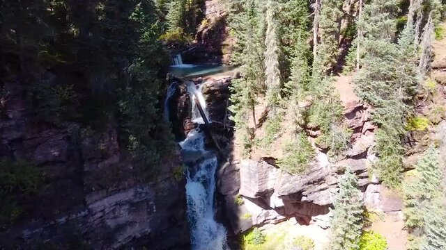 Aerial through two waterfalls in gorge surrounded by pine trees