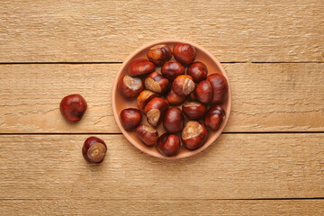 Horse chestnuts in bowl on wooden table. Autumn nature harvest. Top view with copy space.