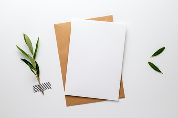 Blank greeting, invitation, congratulation or condolence card beside an olive branch (symbol for life, peace, love and loyalty), fixed on a white desk with washi tape. Top view, flat lay, copy space.