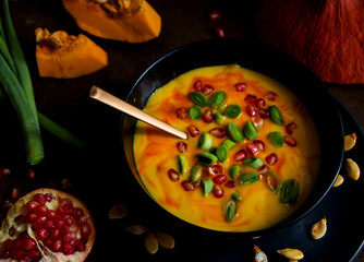 herbstlich cemige kürbissuppe mit granatapfelkernen und frühlingszwiebeln vor dunklen hintergrund