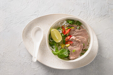 Pho Bo traditional Soup with beef, rice noodles, ginger, lime, chili pepper in bowl on white...