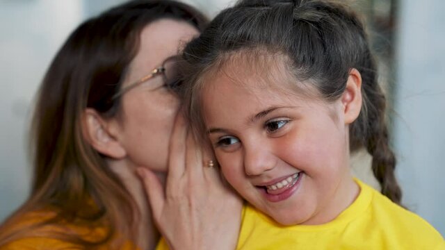 Mom and daughter are happy family. Girl whispers secret to her mother in her ear. Mom communicates with her daughter. Happy family concept. Mom whispers a secret in girl ear. Family games and fun.