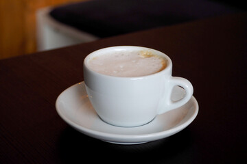 a natural cappuccino in a white cup and saucer stands on a black table in a restaurant. side view