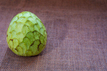 Close-up of a custard apple on rough fabric background, with copy space.