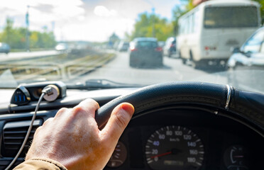 close up, the driver hand on the steering wheel of the car while driving on a suburban highway in a traffic jam in bright sunny weather and in the blinding light of the sun