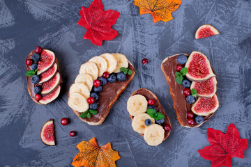 Sweet sandwiches assortment with chocolate nut butter, fig, blueberry, banana and cranberry on the gray table. Top view