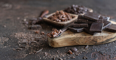 Composition of chocolate pieces, drops and chips on dark concrete background. Background with different kind of chocolate.
