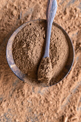 Carob powder in wooden bowl on dark concrete background. Substitute for cocoa. Healthy food concept. Top view.