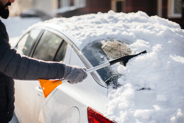 A young man cleans his car after a snowfall on a sunny, frosty day.