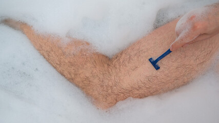 Funny picture of a man taking a relaxing bath and shaving his legs. Close-up of male feet in a bubble bath. Top view.