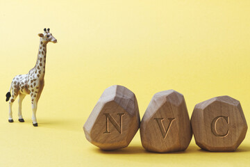 Letters NVC written on wooden irregular blocks with giraffe animal toy. Non-violent communication...