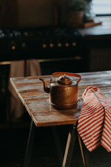 Vertical shot of steel kettle on wooden table in cozy room. Old ancient aluminium teapot to make tea. Vintage houseware.