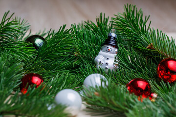 Christmas decorations made of glass. Snowman on the background of fir branches. Postcard for Christmas.