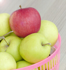 inside a basket of ripe yellow apples stands a large red apple,