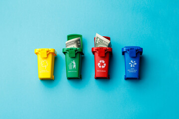 The concept of the collapse of the dollar. Wasted money is the same as being thrown in the trash. Trash cans of different colors with the recycle logo with discarded money on a turquoise background