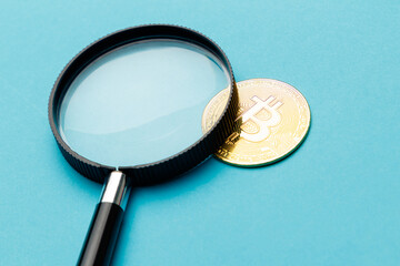 The magnifying glass lies on bitcoin, virtual money, cryptocurrency on a turquoise background. Bitcoin is under close surveillance. Side view from above. A place to copy. Close-up