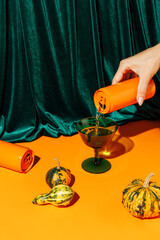 Orange pumpkins and a woman's hand pouring a beverage drink from an orange can against plush velvet...