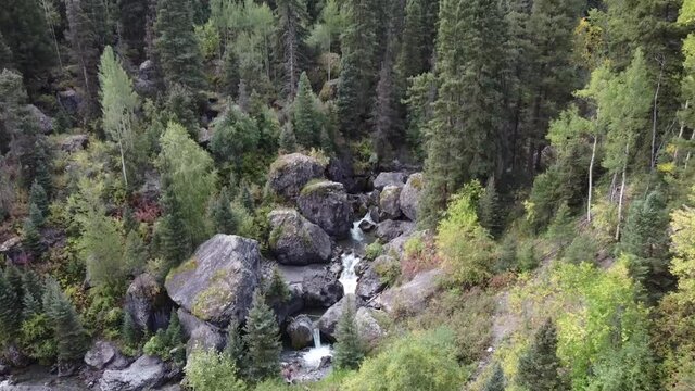 Aerial towards unique waterfall in pine tree forest through giant boulders