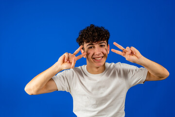 Young casual man making victory hand gesture and smiling on blue background